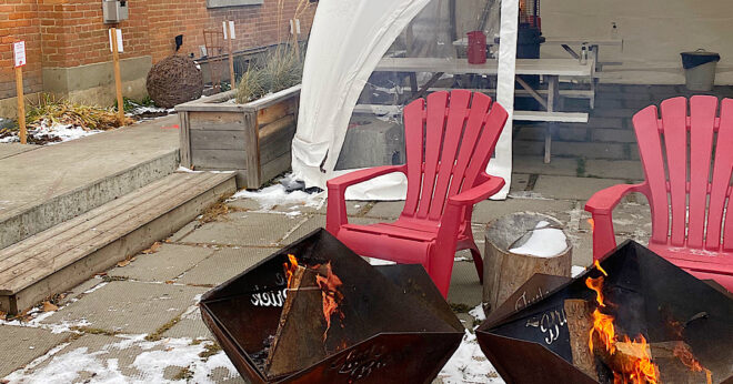 Two red chairs in front of a metal fire pit on a wintry patio.
