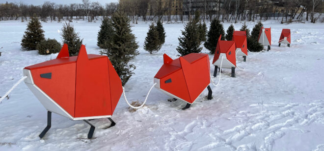 An outdoor sculptural display of boxy red animals in the snow.